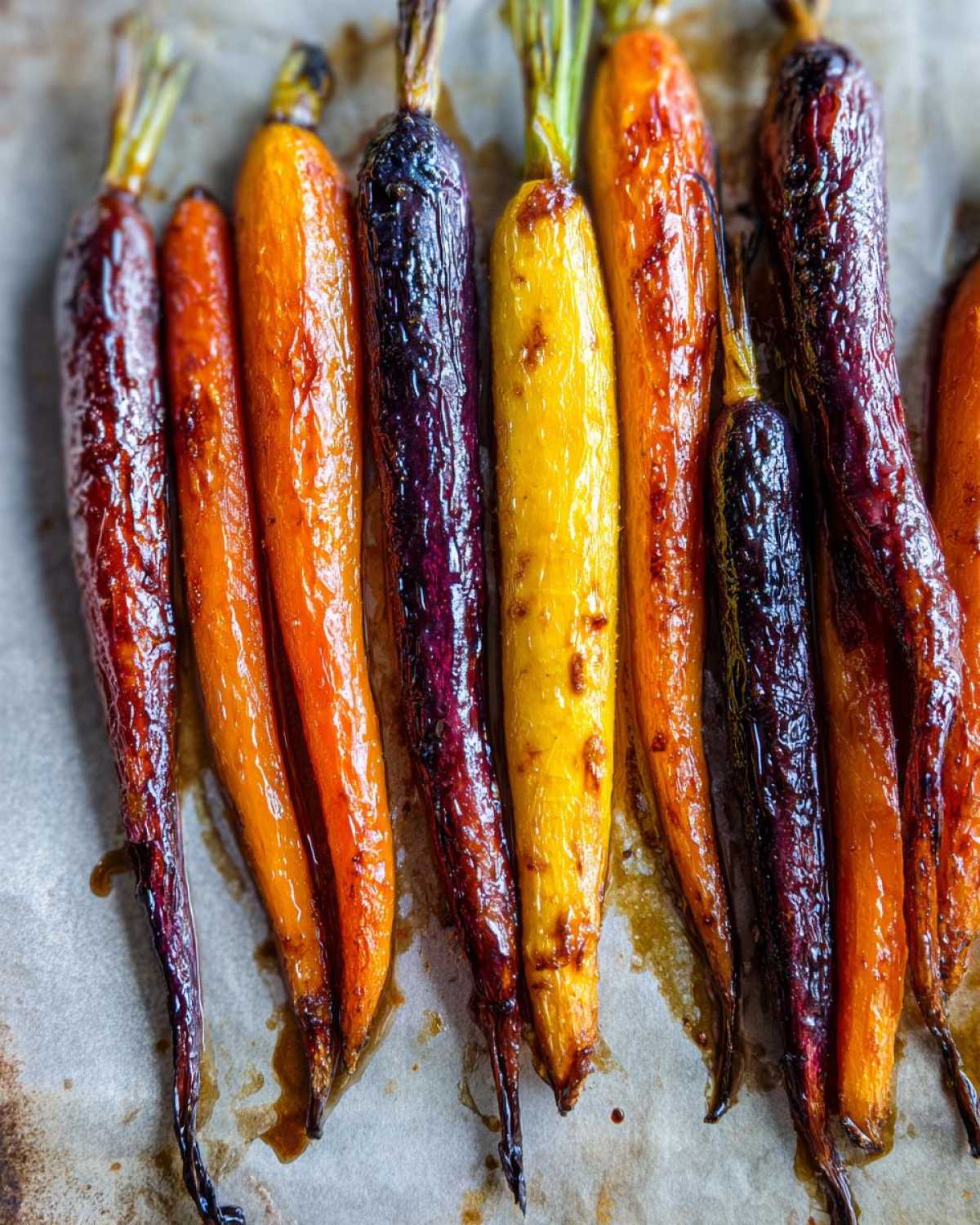 Close-up of glossy, caramelized Sheet Pan Roasted Rainbow Carrots with Honey on parchment paper.