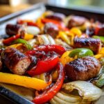 Close-up of browned sausage pieces mixed with roasted red, yellow, and green peppers and onions on a sheet pan.