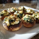 Close-up of baked Spinach and Feta Stuffed Mushrooms piled high with cheesy filling on a white platter.