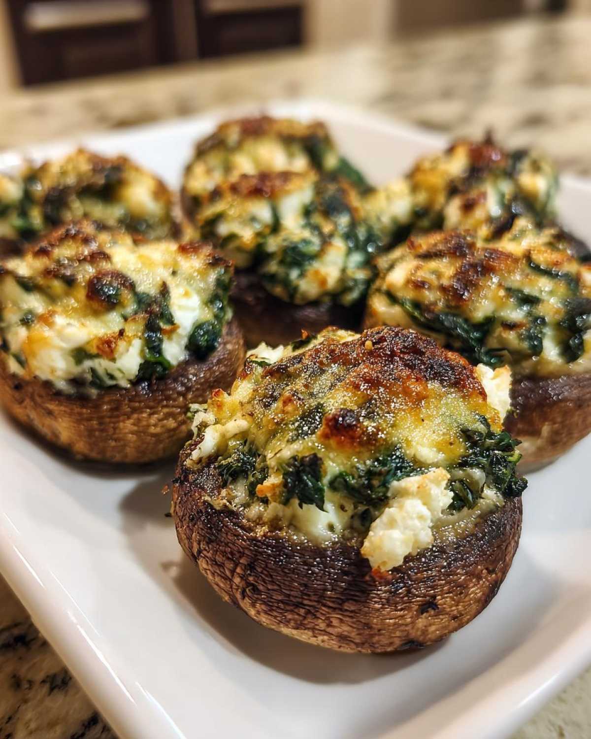 Close-up of baked Spinach and Feta Stuffed Mushrooms with golden-brown, cheesy tops served on a white platter.