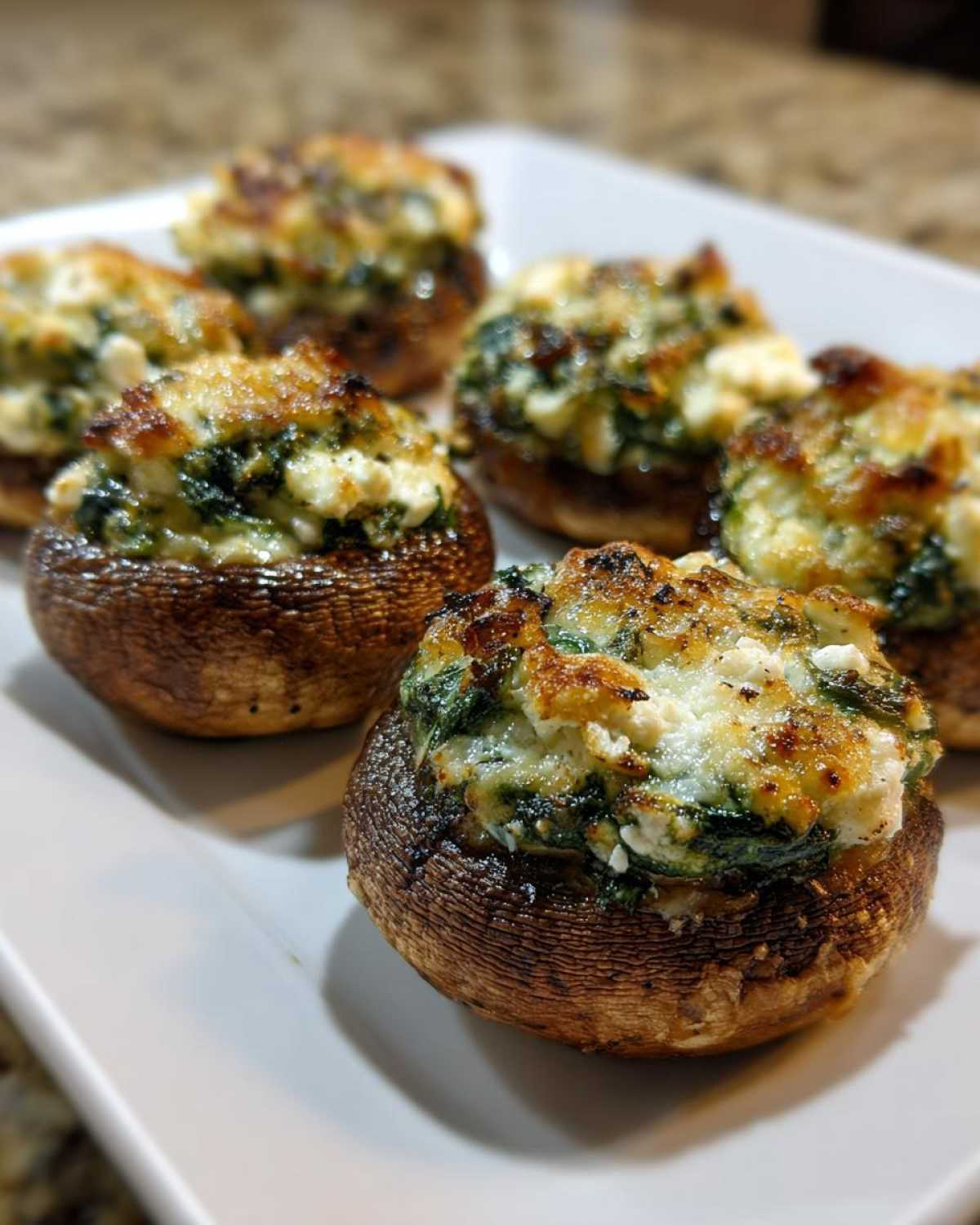 Close-up of several baked Spinach and Feta Stuffed Mushrooms with golden-brown, cheesy tops on a white plate.