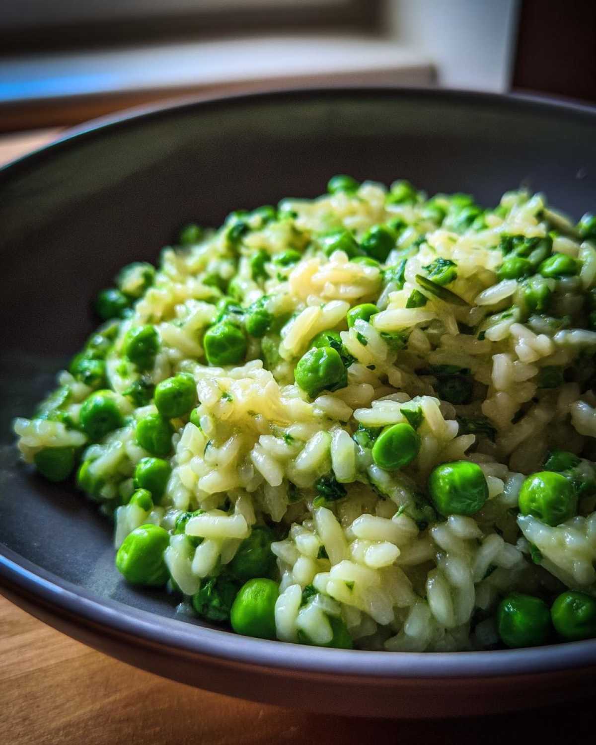 Close-up of creamy Spring Pea and Mint Risotto with bright green peas served in a dark bowl.