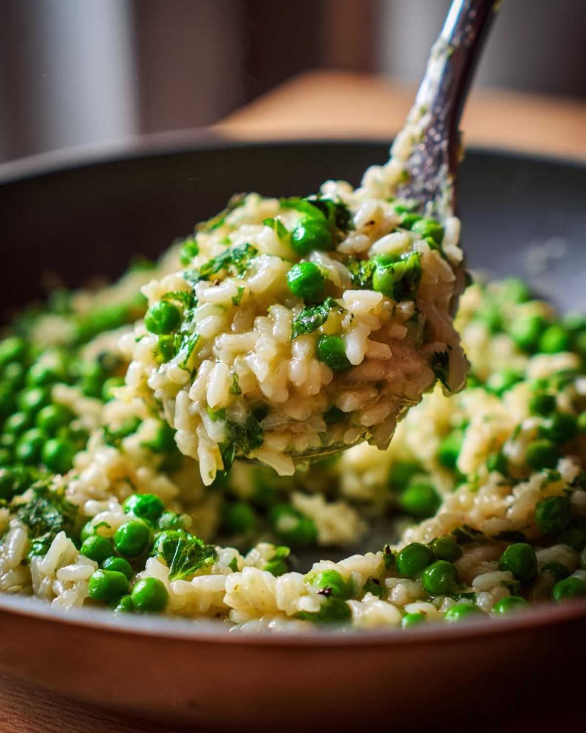 A spoonful of creamy Spring Pea and Mint Risotto being lifted from a dark pan.