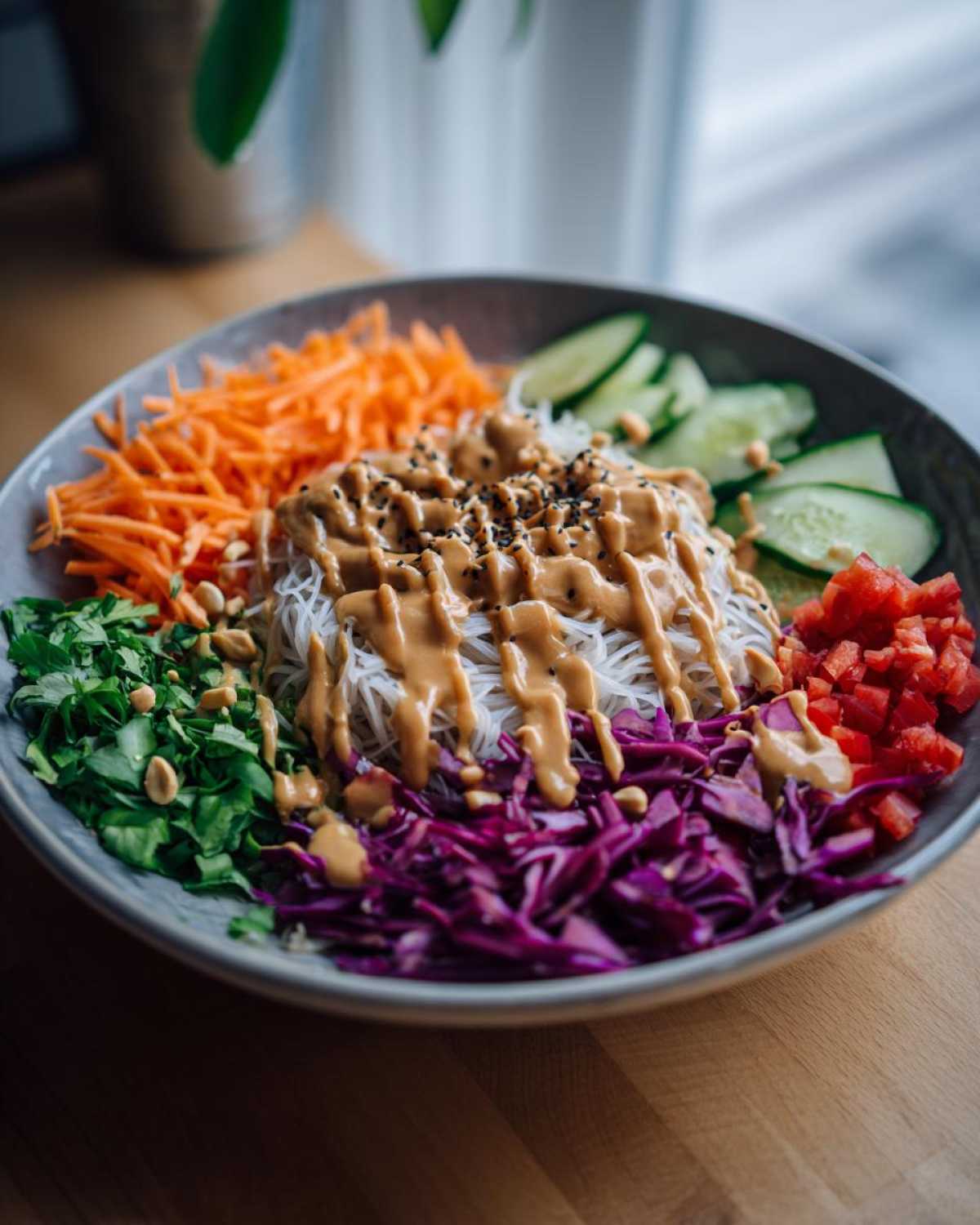 A colorful Spring Roll Bowl with peanut sauce drizzled over rice noodles and surrounded by shredded carrots, cucumbers, and cabbage.