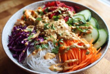 A close-up of a colorful Spring Roll Bowl with Peanut Sauce, featuring vermicelli noodles, shredded carrots, cabbage, and cucumber.