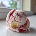 A close-up scoop of homemade Strawberry Banana Ice Cream showing swirls of pink and white, with visible pieces of strawberry and banana.