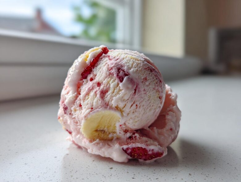 A close-up scoop of homemade Strawberry Banana Ice Cream showing swirls of pink and white, with visible pieces of strawberry and banana.