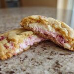Close-up of Strawberry Cheesecake Stuffed Cookies cut in half showing the creamy pink and white filling.