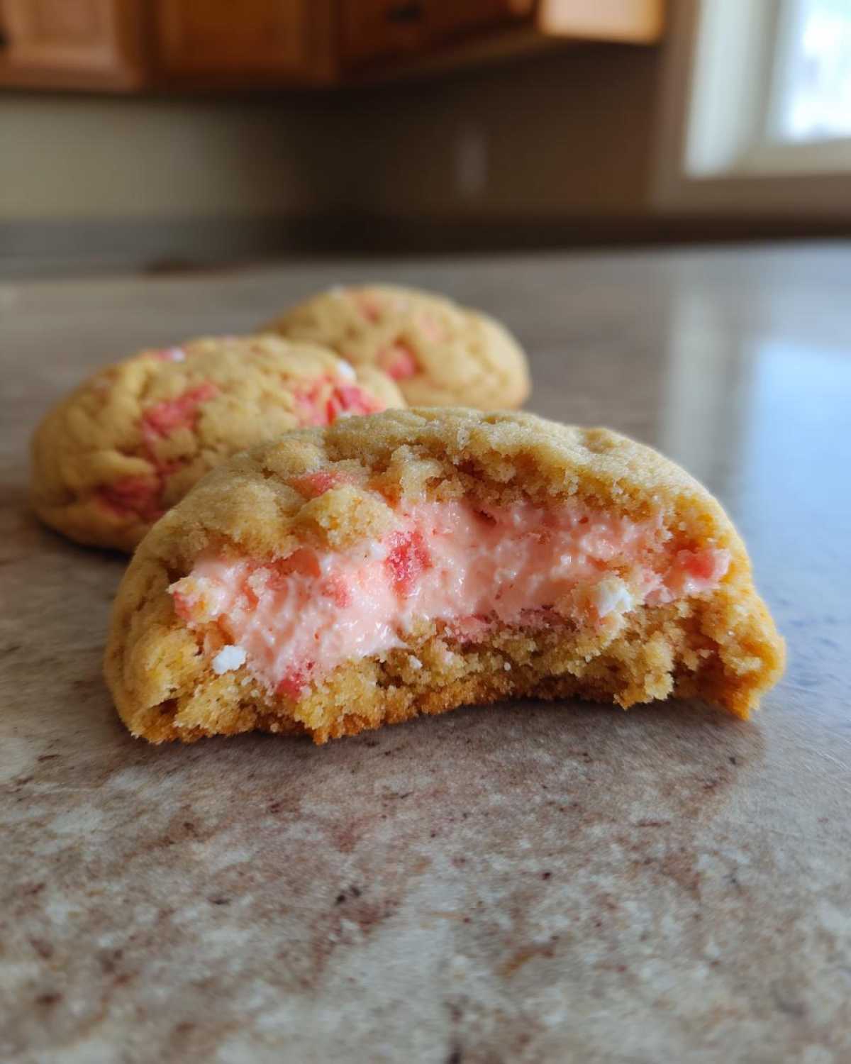 Close-up of a Strawberry Cheesecake Stuffed Cookie cut in half, showing the creamy pink filling inside the soft cookie.