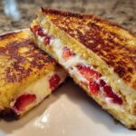 Two halves of golden brown Strawberry Cream Cheese Stuffed French Toast showing the creamy filling and sliced strawberries.