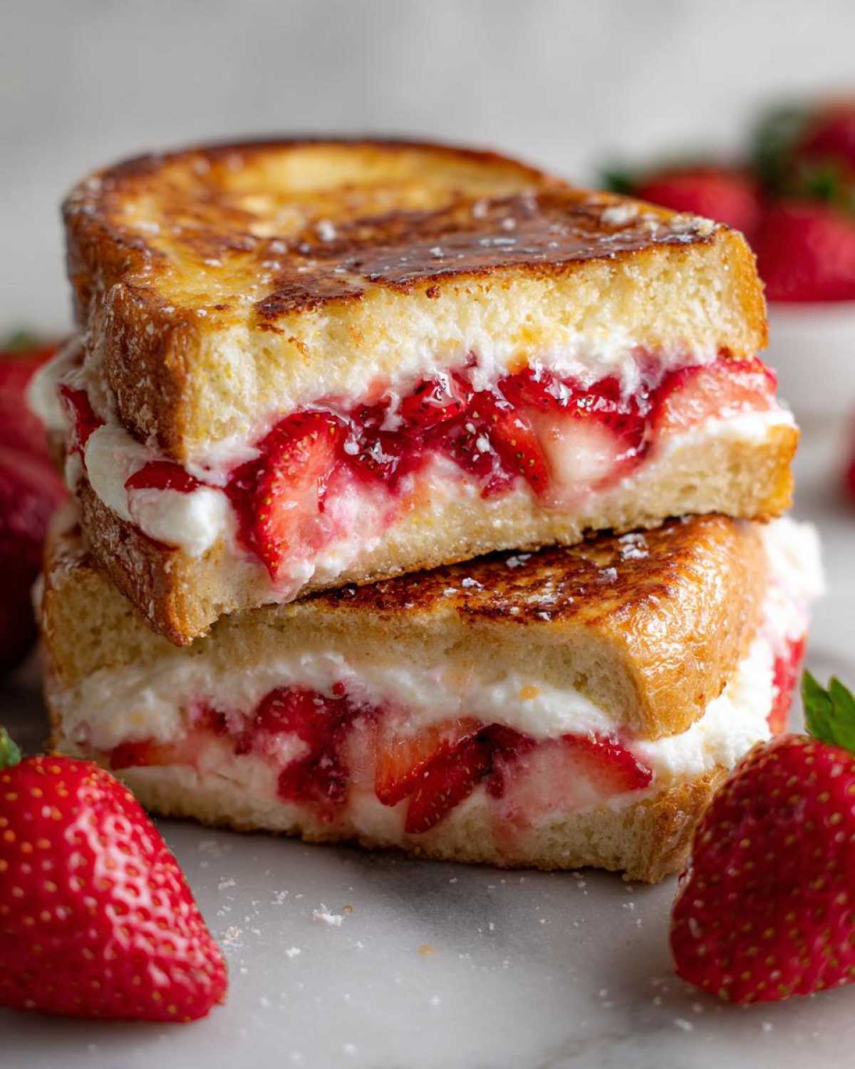 A stack of two halves of Strawberry Cream Cheese Stuffed French Toast, showing the creamy filling and sliced strawberries.