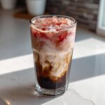 Close-up of a tall glass showing distinct layers of dark cold brew, creamy milk, and strawberry topping in a Strawberry Cream Cold Brew.