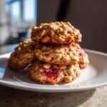 A stack of four golden Strawberry Oatmeal Breakfast Cookies with visible strawberry filling on a white plate.