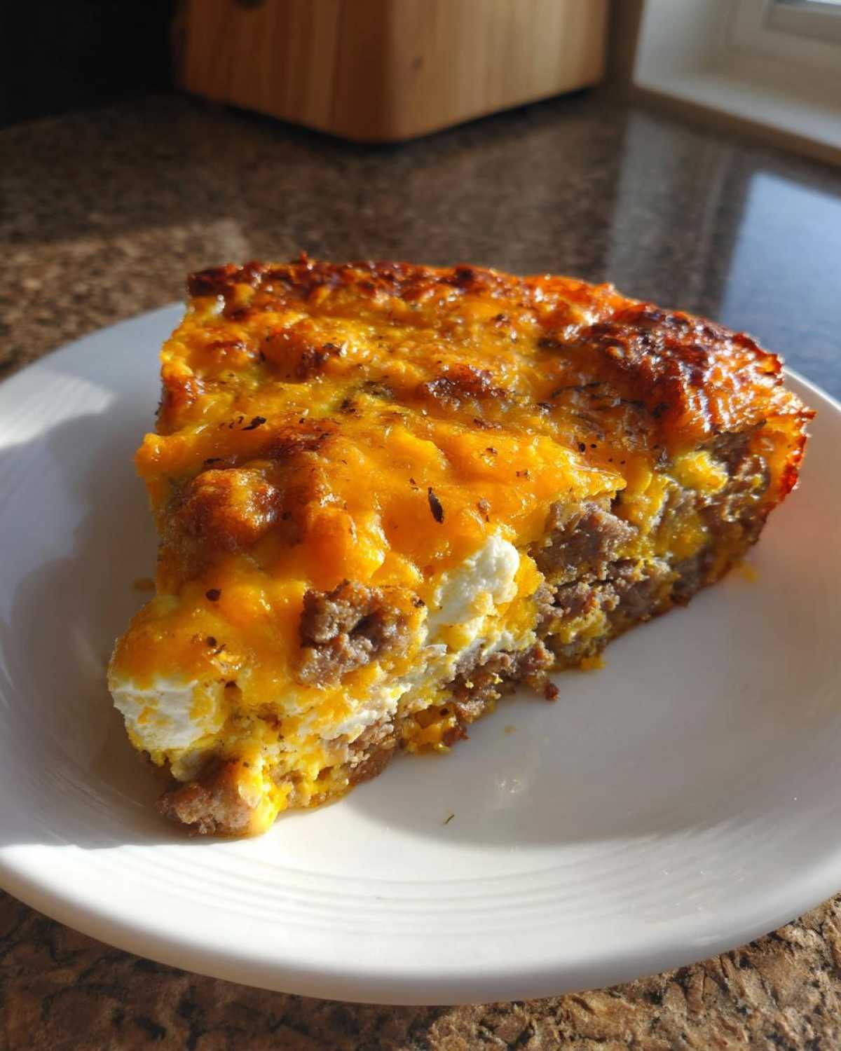 A close-up slice of Tater Tot Breakfast Casserole featuring layers of sausage, eggs, and melted cheddar cheese.