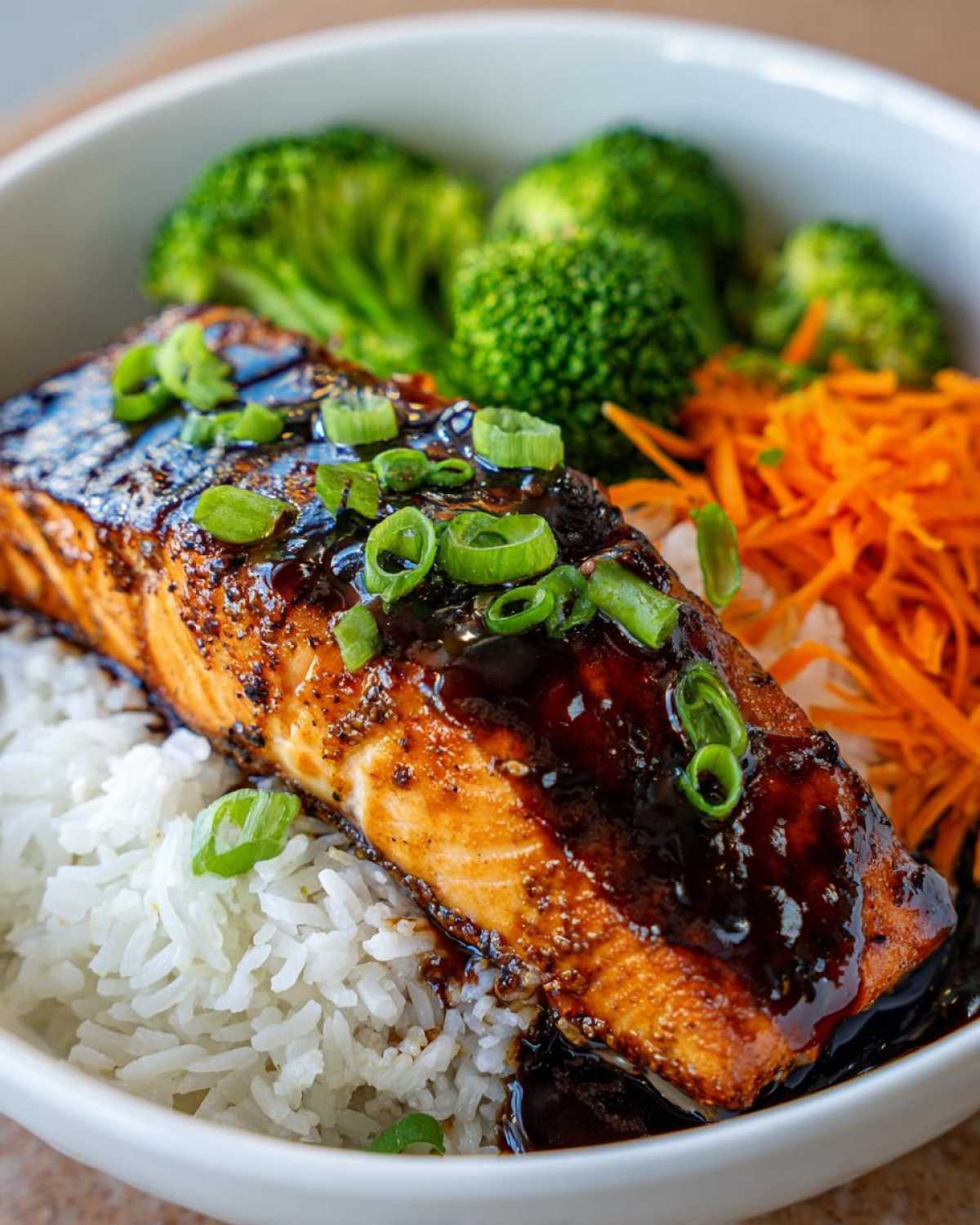 Close-up of a Teriyaki Salmon Rice Bowl featuring glazed salmon, white rice, broccoli, and shredded carrots.