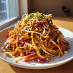 A tall serving of Thai Peanut Noodles with Crunchy Veggies, topped with peanuts and green onions.