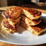 Close-up of a stack of fluffy Vegan Banana Oat Pancakes, cut open to show the texture.