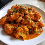 Close-up of vibrant orange Vegan Cauliflower Tikka Masala florets covered in rich sauce and garnished with fresh cilantro.