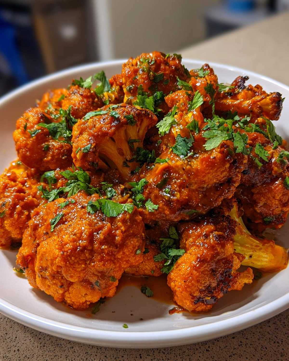 Close-up of roasted cauliflower florets coated in rich, orange Vegan Cauliflower Tikka Masala sauce and topped with fresh cilantro.