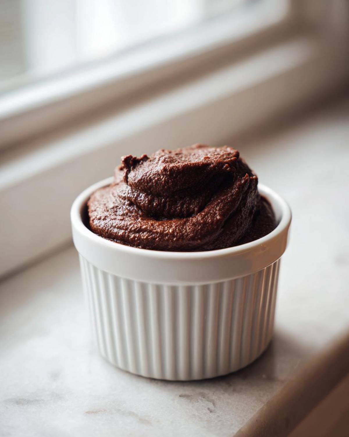 A close-up of rich, dark Vegan Chocolate Avocado Mousse swirled high in a white ceramic ramekin.