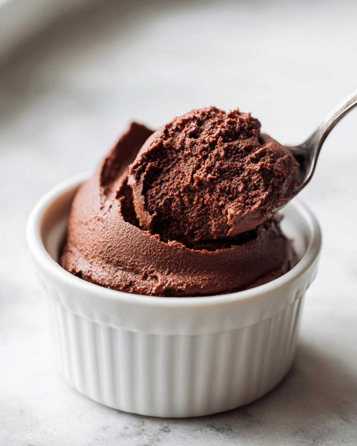 A spoonful of rich, dark Vegan Chocolate Avocado Mousse being lifted from a small white ramekin.