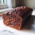 Close-up of a moist, dark Vegan Chocolate Banana Bread loaf topped with chocolate chips.