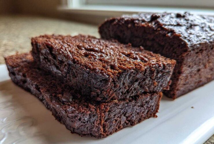 Close-up of moist slices of rich Vegan Chocolate Banana Bread stacked on a white serving platter.