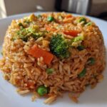 A perfectly molded serving of Vegetable Fried Rice with Sesame Ginger Sauce, featuring broccoli, carrots, and peas.