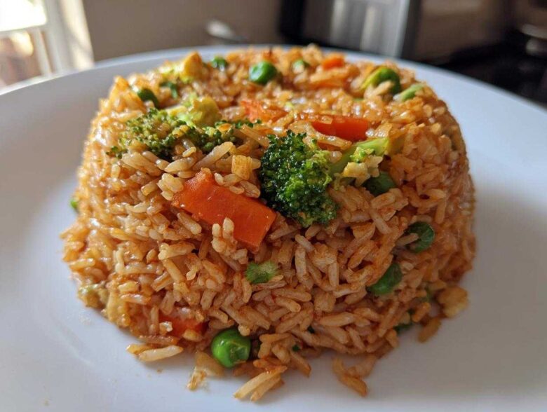 A perfectly molded serving of Vegetable Fried Rice with Sesame Ginger Sauce, featuring broccoli, carrots, and peas.