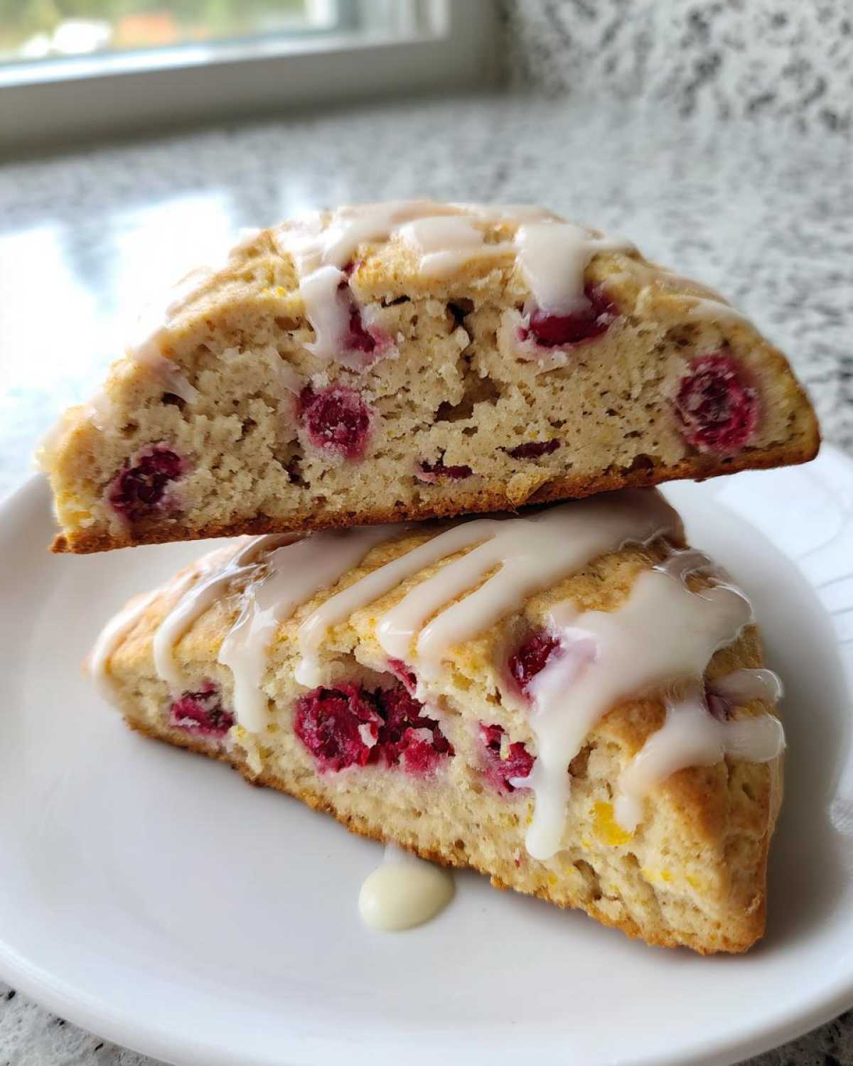 Two halves of a White Chocolate Raspberry Scone stacked, showing the moist interior filled with raspberries and drizzled with white chocolate glaze.