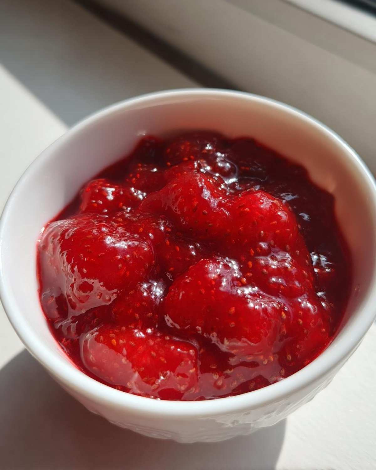 Close-up of bright red, chunky 10-Minute Strawberry Chia Jam served in a small white bowl.