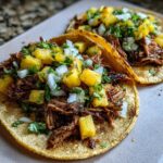 Close-up of two Al Pastor Pork Tacos topped generously with diced pineapple, white onion, and cilantro.