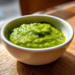 Close-up of vibrant green Avocado Tomatillo Salsa Verde served in a small white bowl on a wooden surface.