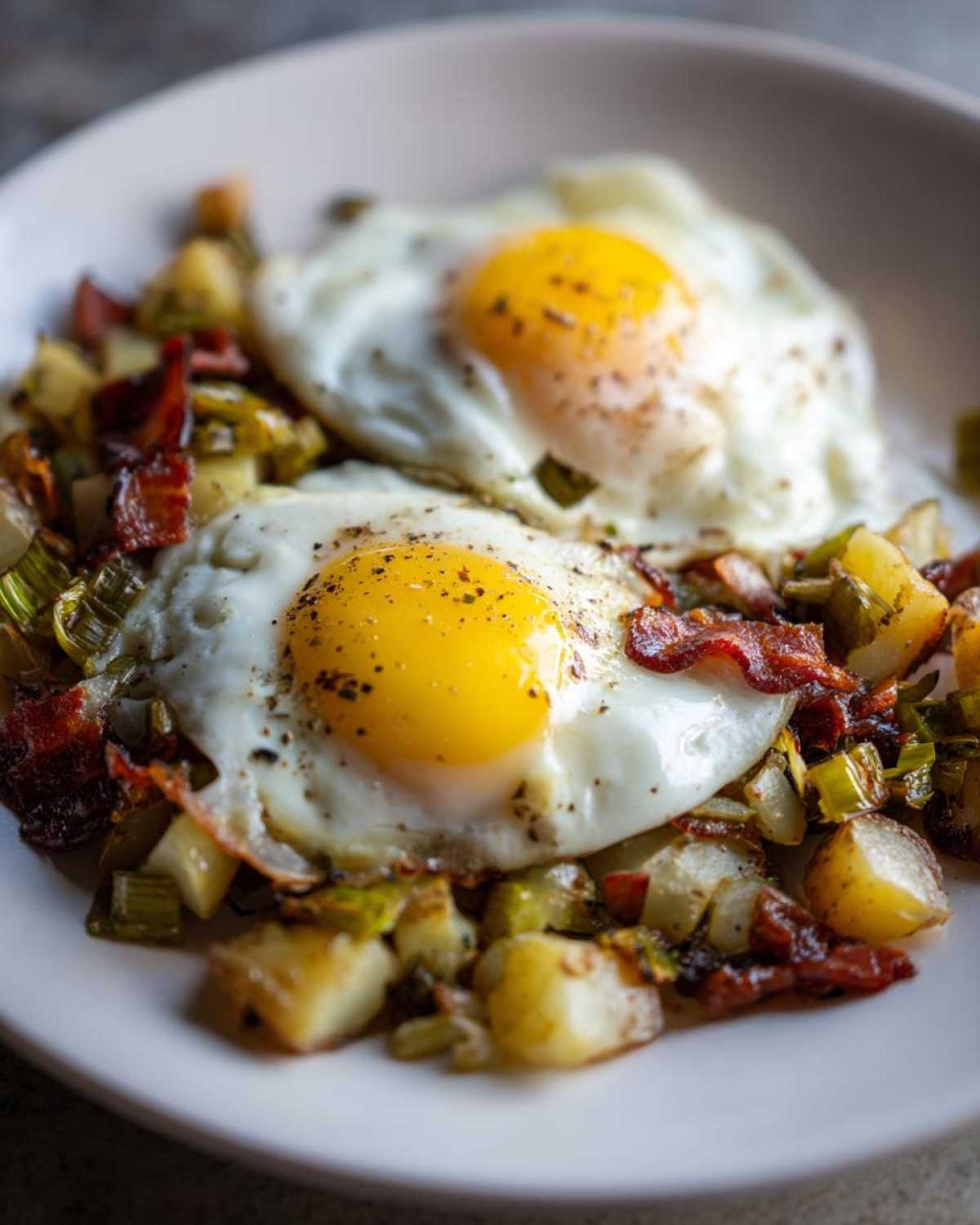 Close-up of Bacon Leek Breakfast Hash topped with two perfectly cooked sunny-side-up eggs.
