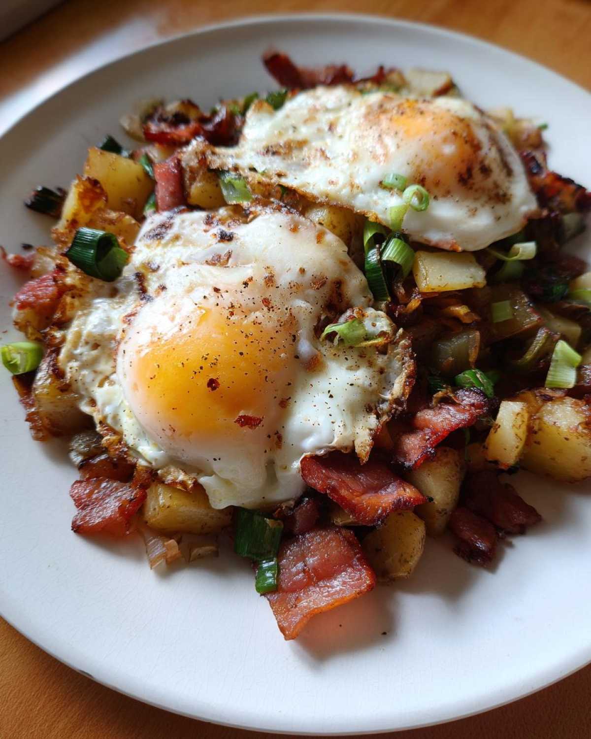 Close-up of Bacon Leek Breakfast Hash topped with two sunny-side-up eggs and green onions.