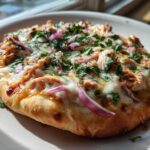 A close-up of a freshly baked BBQ Chicken Flatbread Pizza topped with melted cheese, shredded chicken, red onion, and fresh cilantro.