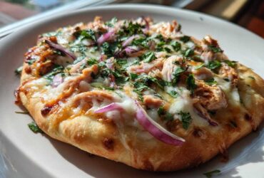 A close-up of a freshly baked BBQ Chicken Flatbread Pizza topped with melted cheese, shredded chicken, red onion, and fresh cilantro.