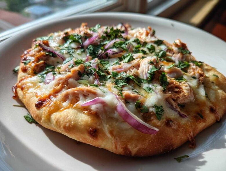 A close-up of a freshly baked BBQ Chicken Flatbread Pizza topped with melted cheese, shredded chicken, red onion, and fresh cilantro.