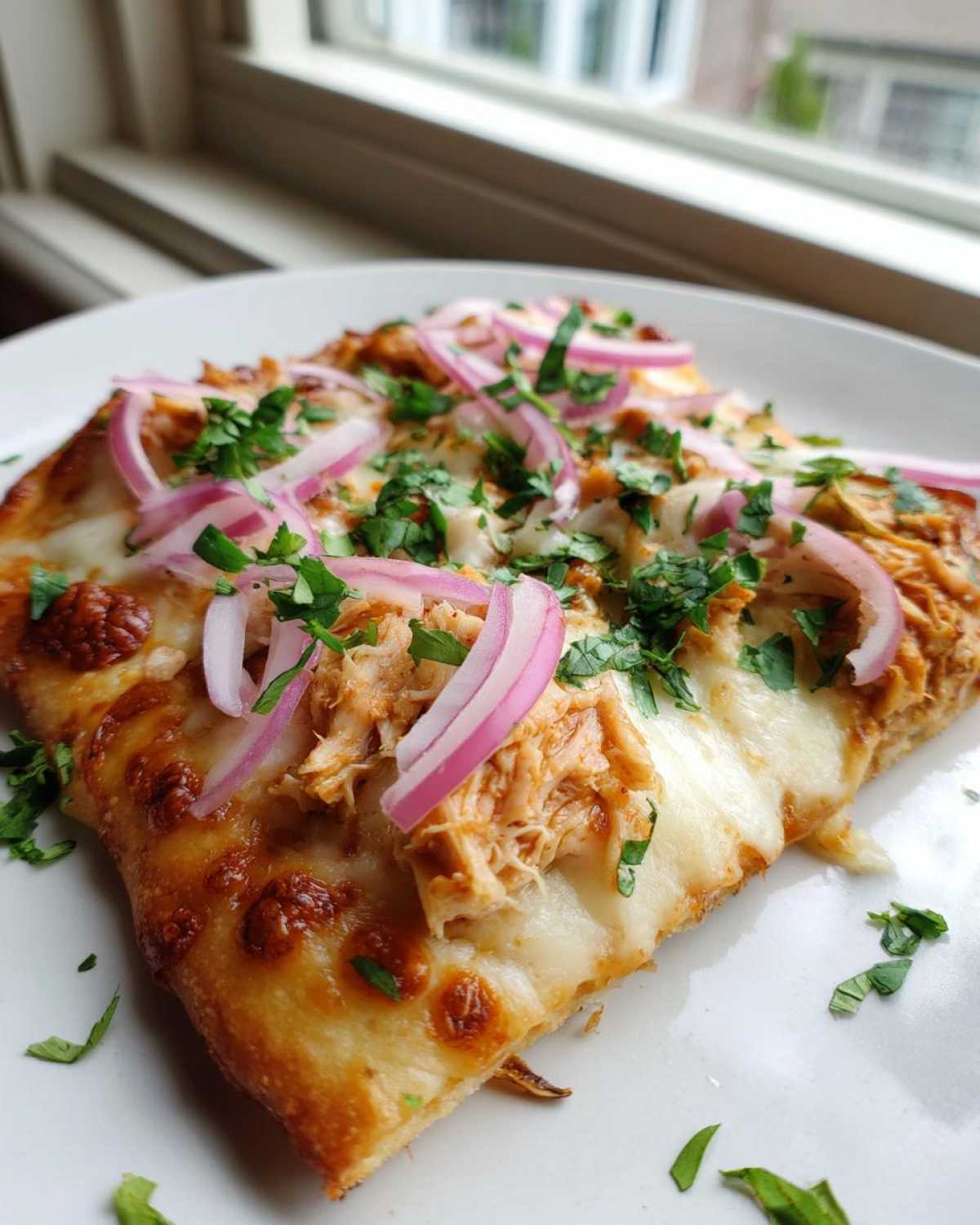 Close-up of a slice of BBQ Chicken Flatbread Pizza topped with melted cheese, shredded chicken, red onion, and fresh parsley.