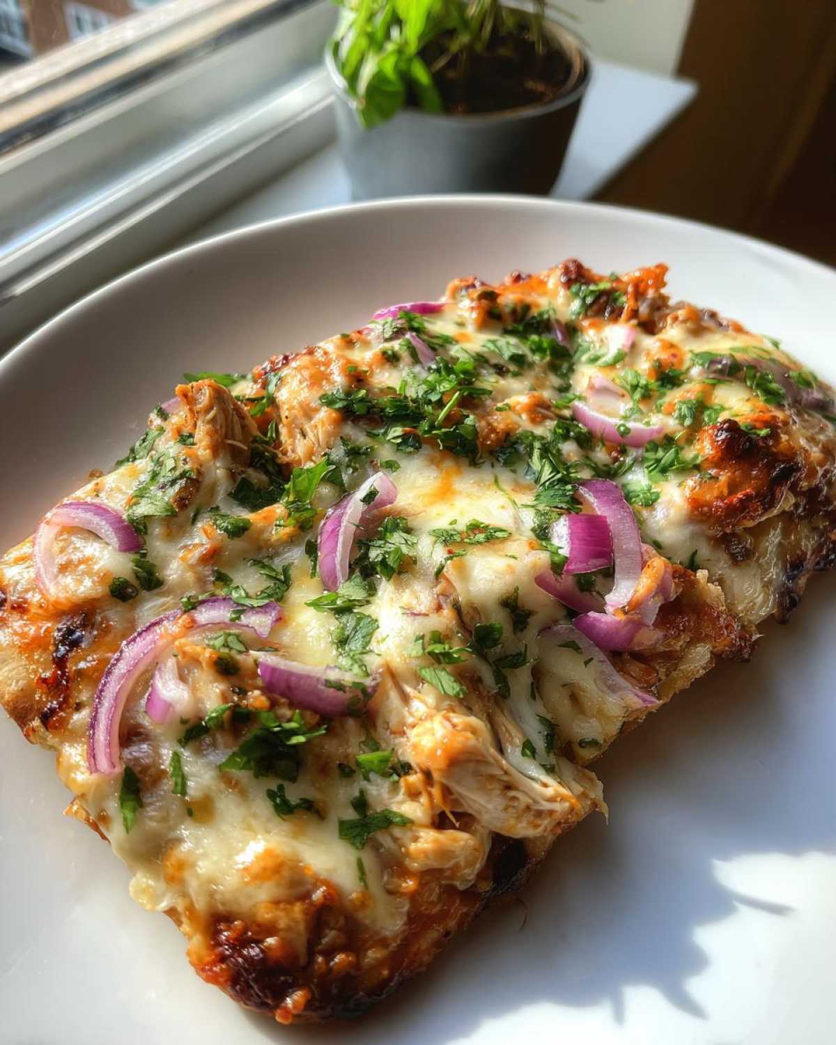 A close-up of a slice of BBQ Chicken Flatbread Pizza topped with melted cheese, red onion, and fresh parsley.