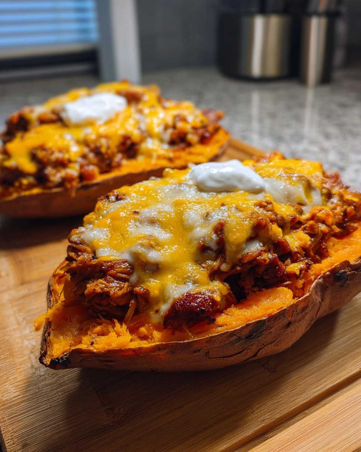 Two halves of baked sweet potatoes generously filled with BBQ Pulled Pork Stuffed Sweet Potatoes, melted cheese, and sour cream.