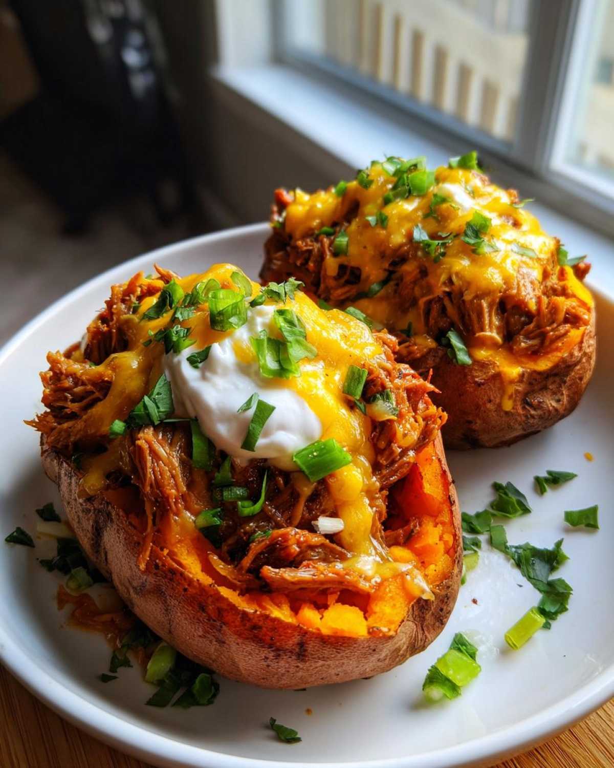 Two halves of baked sweet potatoes filled with BBQ Pulled Pork Stuffed Sweet Potatoes, topped with melted cheese, sour cream, and green onions.