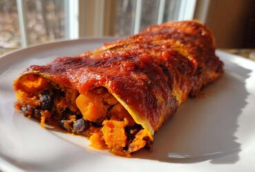 A single serving of Black Bean Sweet Potato Enchiladas covered in red sauce, showing the orange sweet potato and black bean filling.