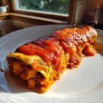 A single serving of Black Bean Sweet Potato Enchiladas covered in bright red enchilada sauce on a white plate.