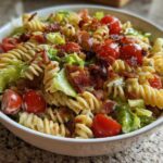 Close-up of a bowl filled with BLT Pasta Salad with Ranch, featuring rotini pasta, cherry tomatoes, lettuce, and bacon bits.