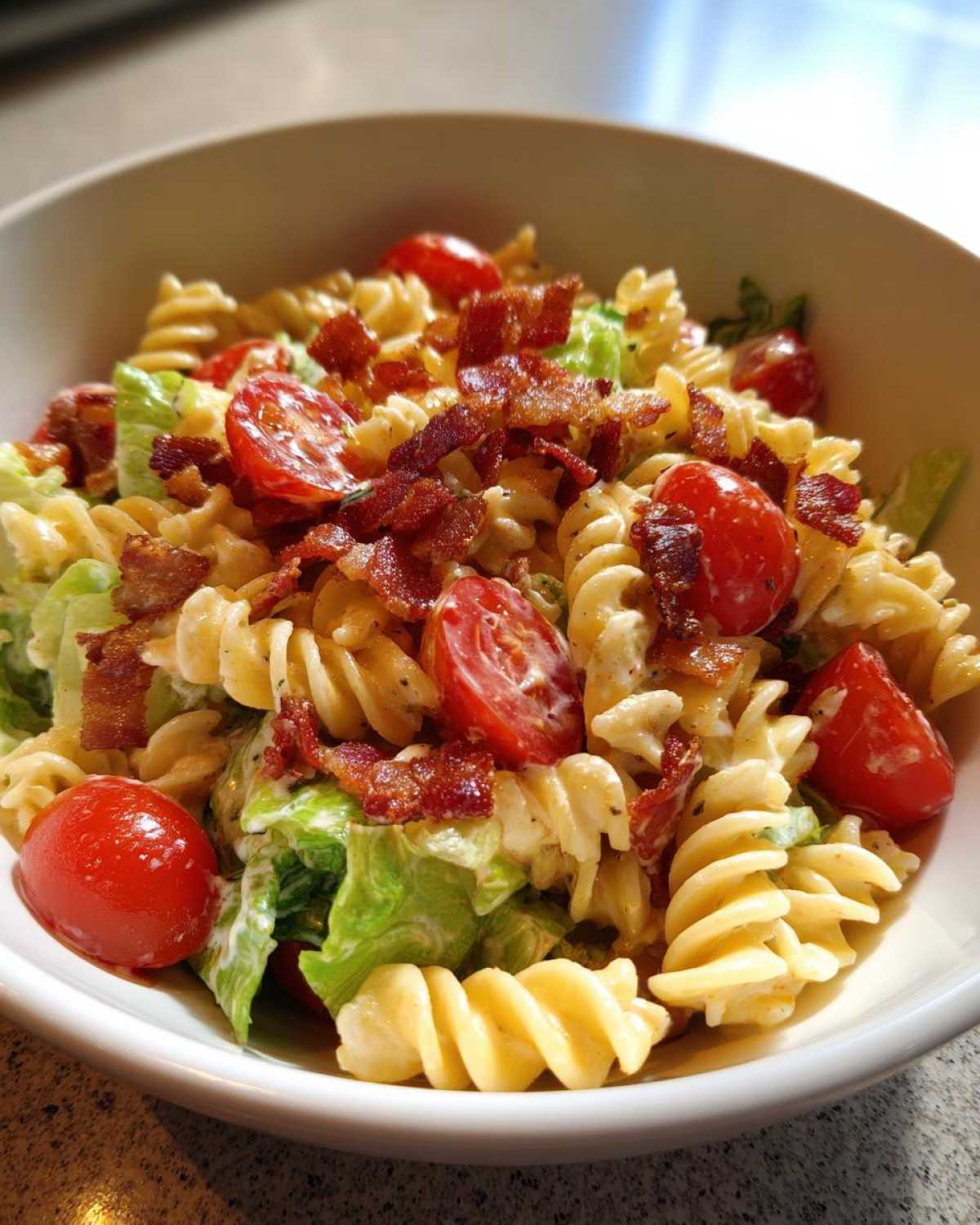 A close-up view of a creamy BLT Pasta Salad with Ranch, featuring rotini pasta, cherry tomatoes, and crispy bacon pieces.