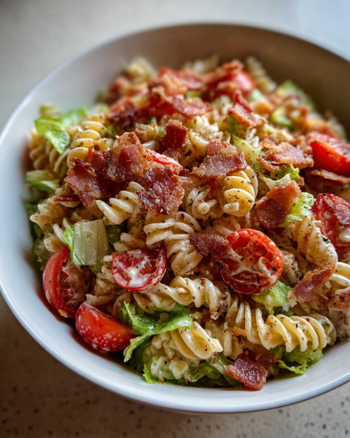 A close-up view of a creamy BLT Pasta Salad with Ranch, featuring rotini pasta, crisp lettuce, cherry tomatoes, and crumbled bacon.