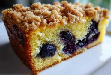 Close-up of a moist slice of Blueberry Almond Coffee Cake showing blueberries baked into the yellow crumb and a thick brown sugar streusel topping.