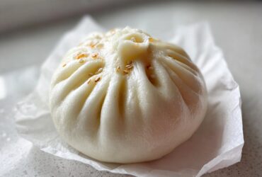 Close-up of a single, fluffy, white Char Siu Mushroom Bao sprinkled with toasted sesame seeds.
