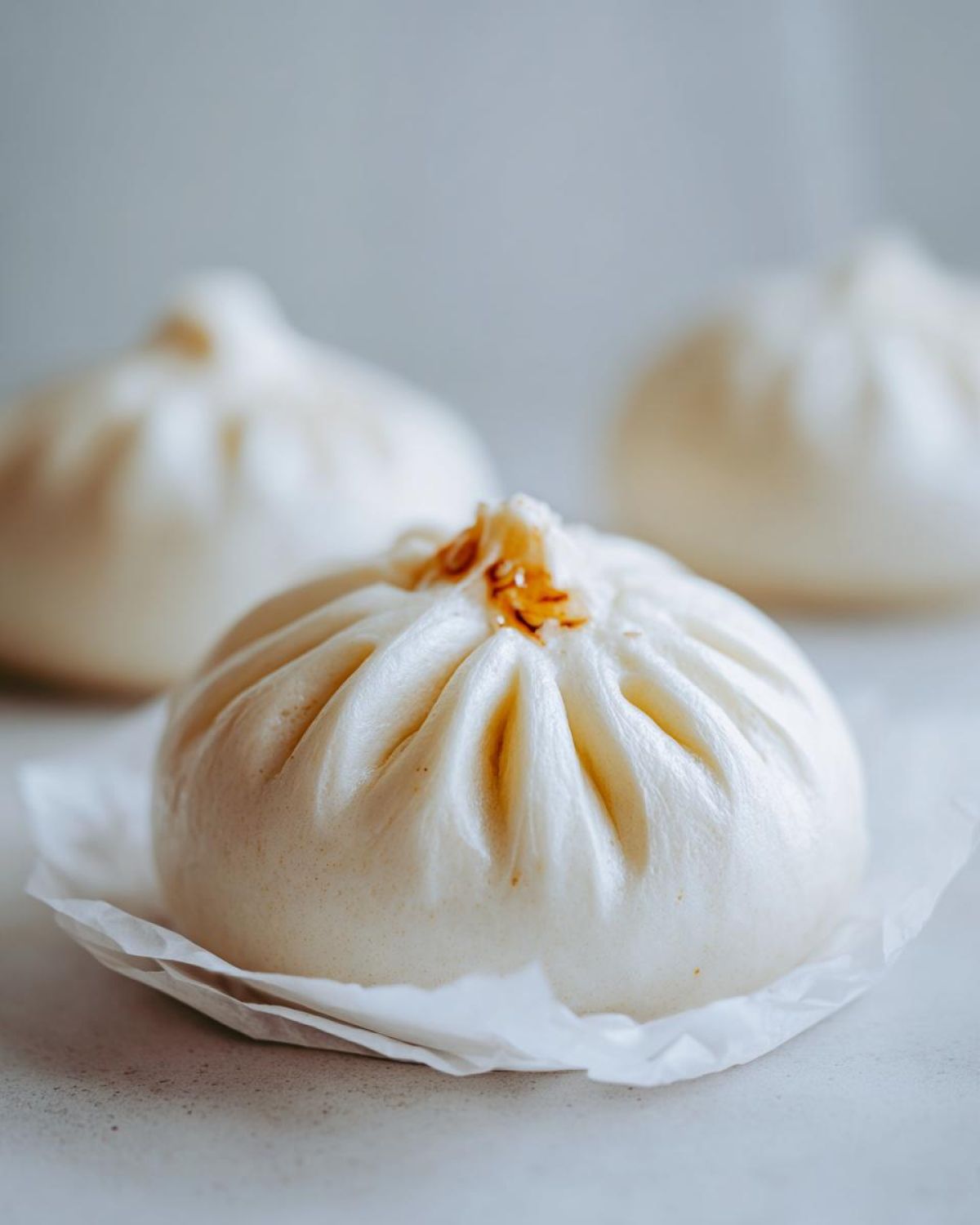 Close-up of a single, fluffy, steamed Char Siu Mushroom Bao resting on a piece of white parchment paper.